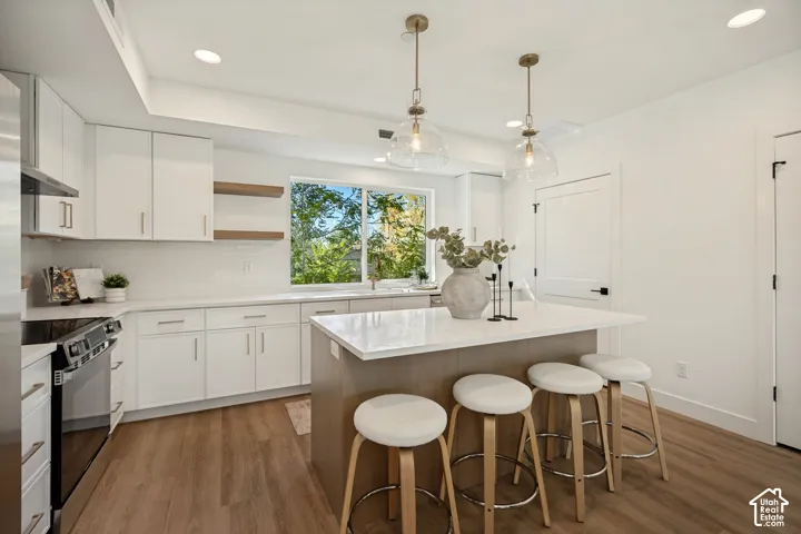 Kitchen featuring shaker-style cabinetry, quartz countertops, a central island with wood-finish paneling, floating wood shelves, and glass globe pendant lighting