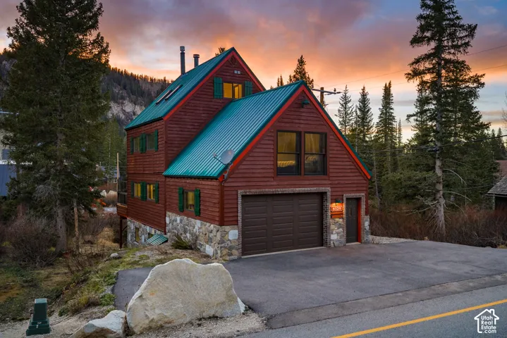 Multi-level residence featuring horizontal wood siding, a green metal roof, stone foundation veneer, skylights, and an attached two-car garage