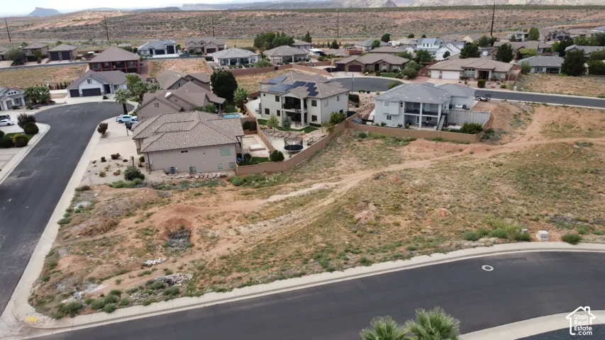 Aerial perspective of a corner residential lot featuring native desert landscaping, paved streets, and expansive mountain terrain
