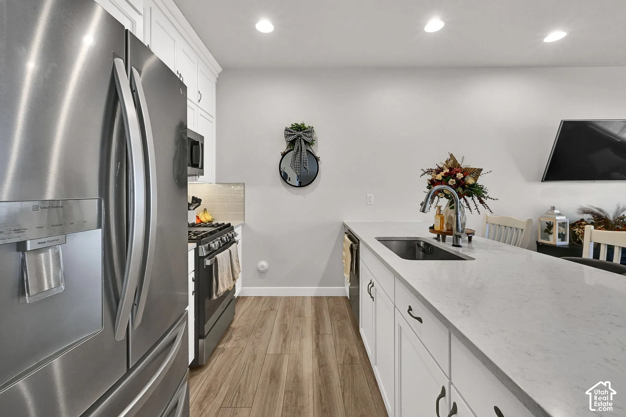 Kitchen featuring white cabinetry, wood-finish flooring, stone-composite countertops, stainless steel appliances, and recessed lighting