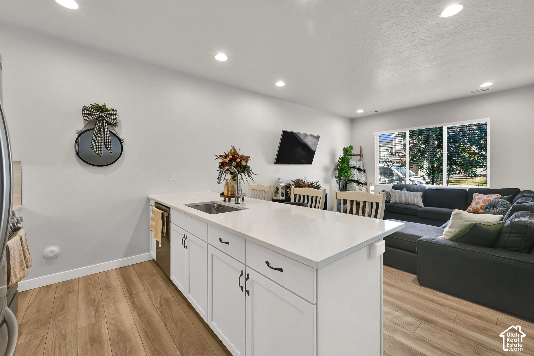Kitchen island featuring white shaker-style cabinetry, quartz countertops, a stainless steel undermount sink, and wood-finish flooring with recessed lighting