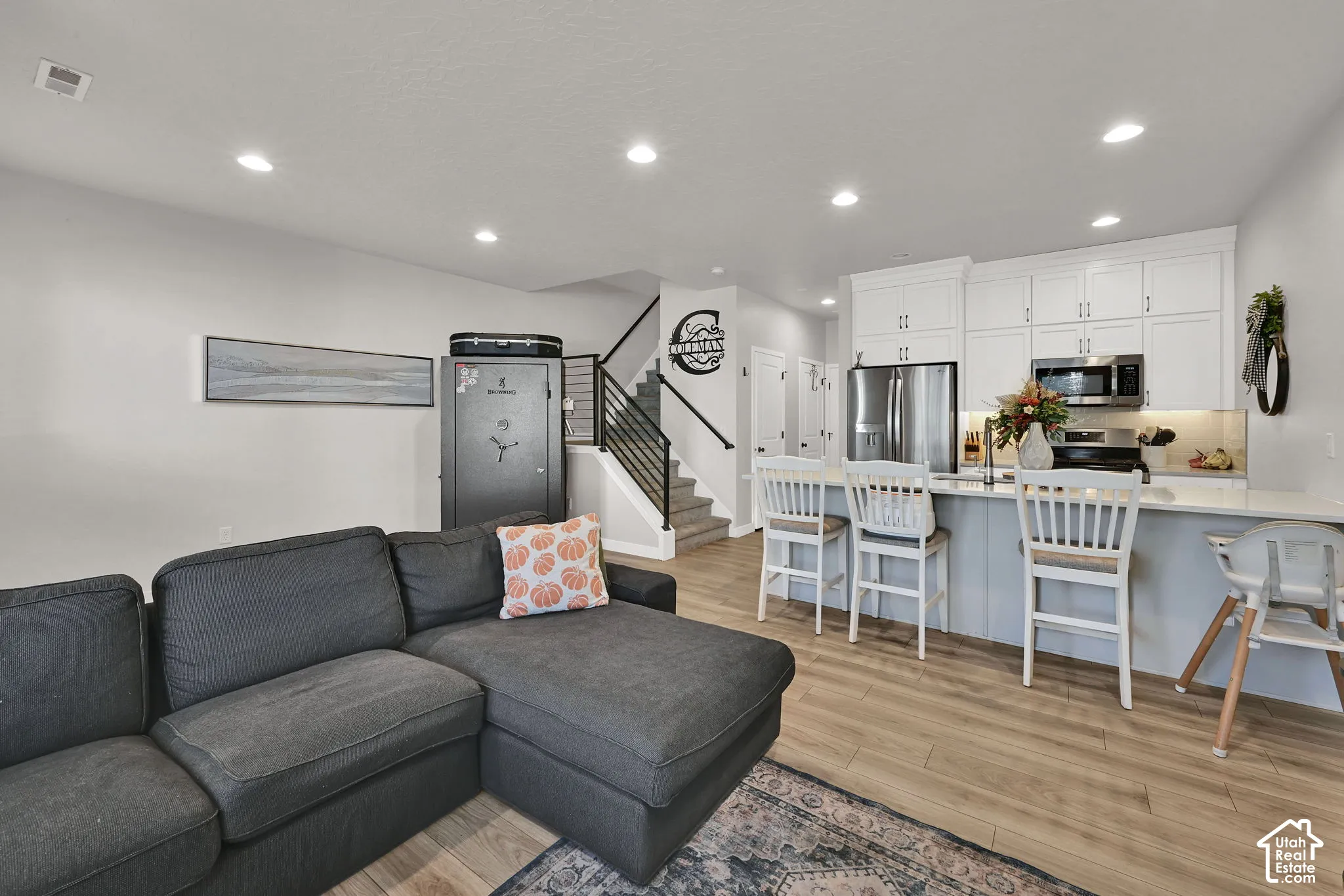 Kitchen featuring white upper cabinetry, stainless steel appliances, breakfast bar island, recessed lighting, and wood-finish flooring
