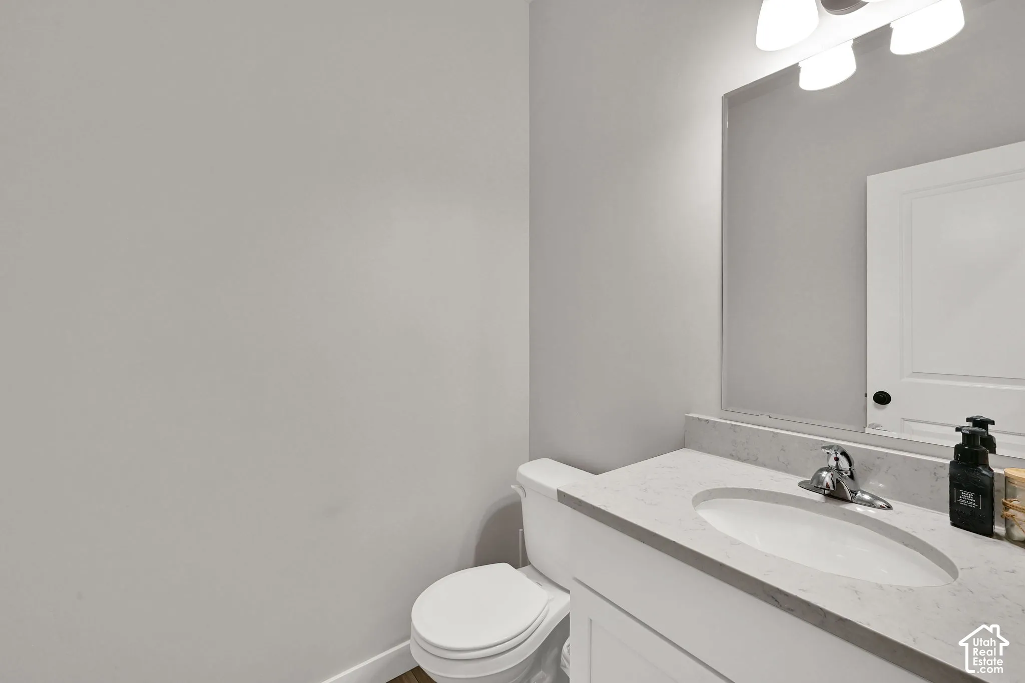 Single-sink vanity with a solid-surface countertop, integrated oval basin, polished chrome faucet, large-format wall mirror, and overhead tri-light fixture