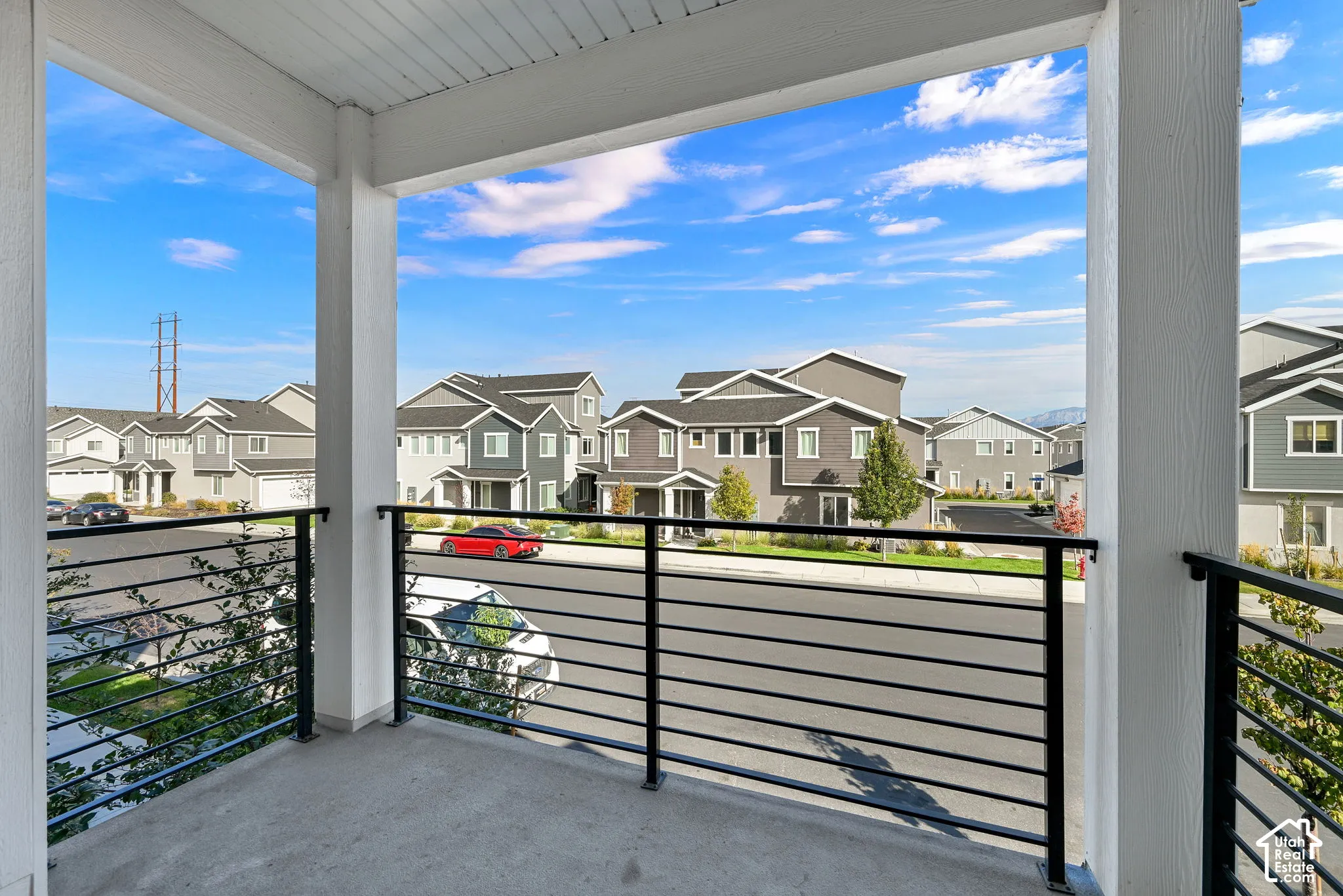 Covered balcony featuring concrete flooring, white structural columns, and a black metal horizontal-bar railing