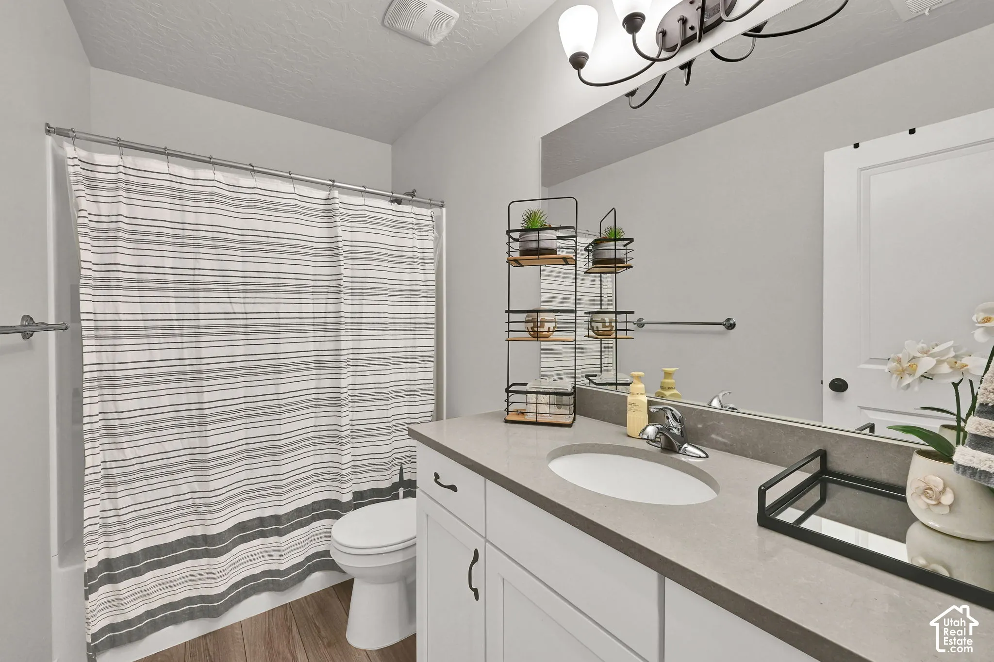 Bathroom featuring a white vanity with a composite countertop, an undermount sink, a full-width mirror, and wood-finish flooring
