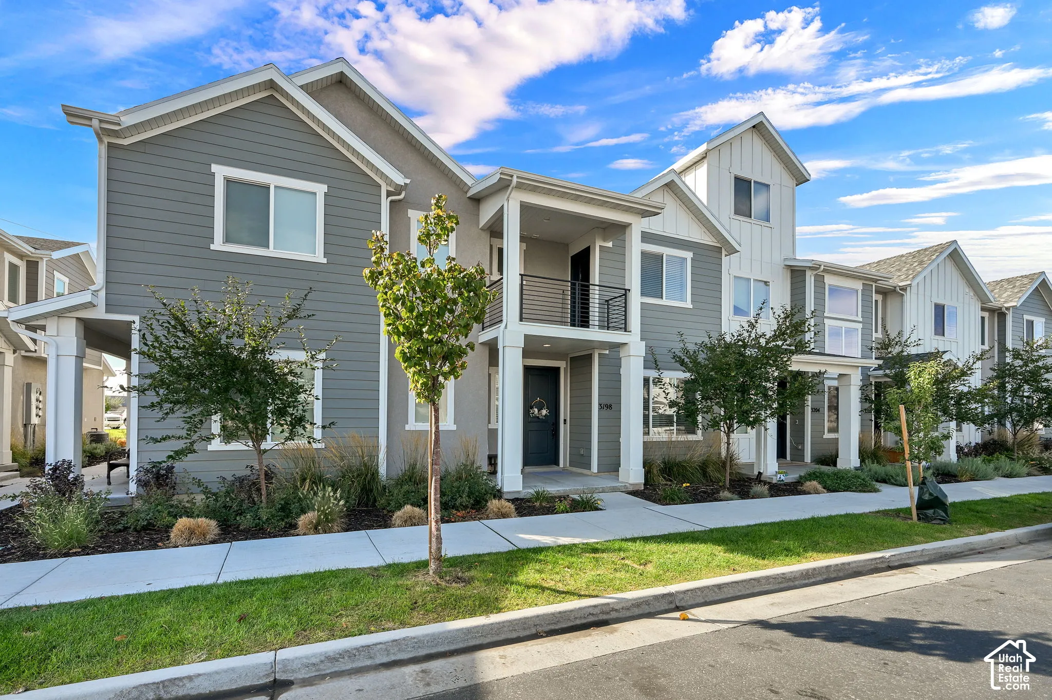 Multi-story exterior featuring a mix of horizontal and vertical siding, a covered entry porch, a second-story balcony with metal railing, and concrete sidewalk access