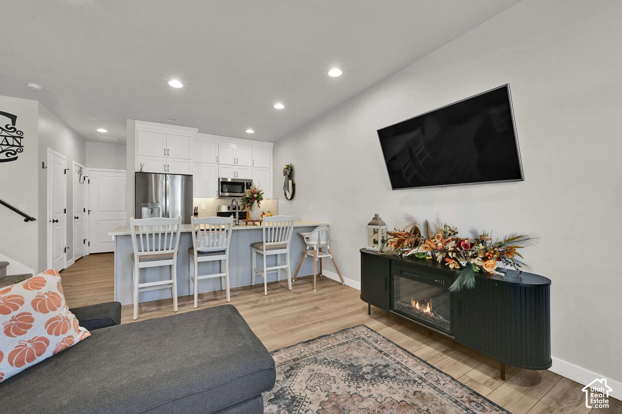 Open-concept kitchen featuring white shaker-style cabinetry, stainless steel appliances, a breakfast bar, and wood-finish flooring with recessed lighting