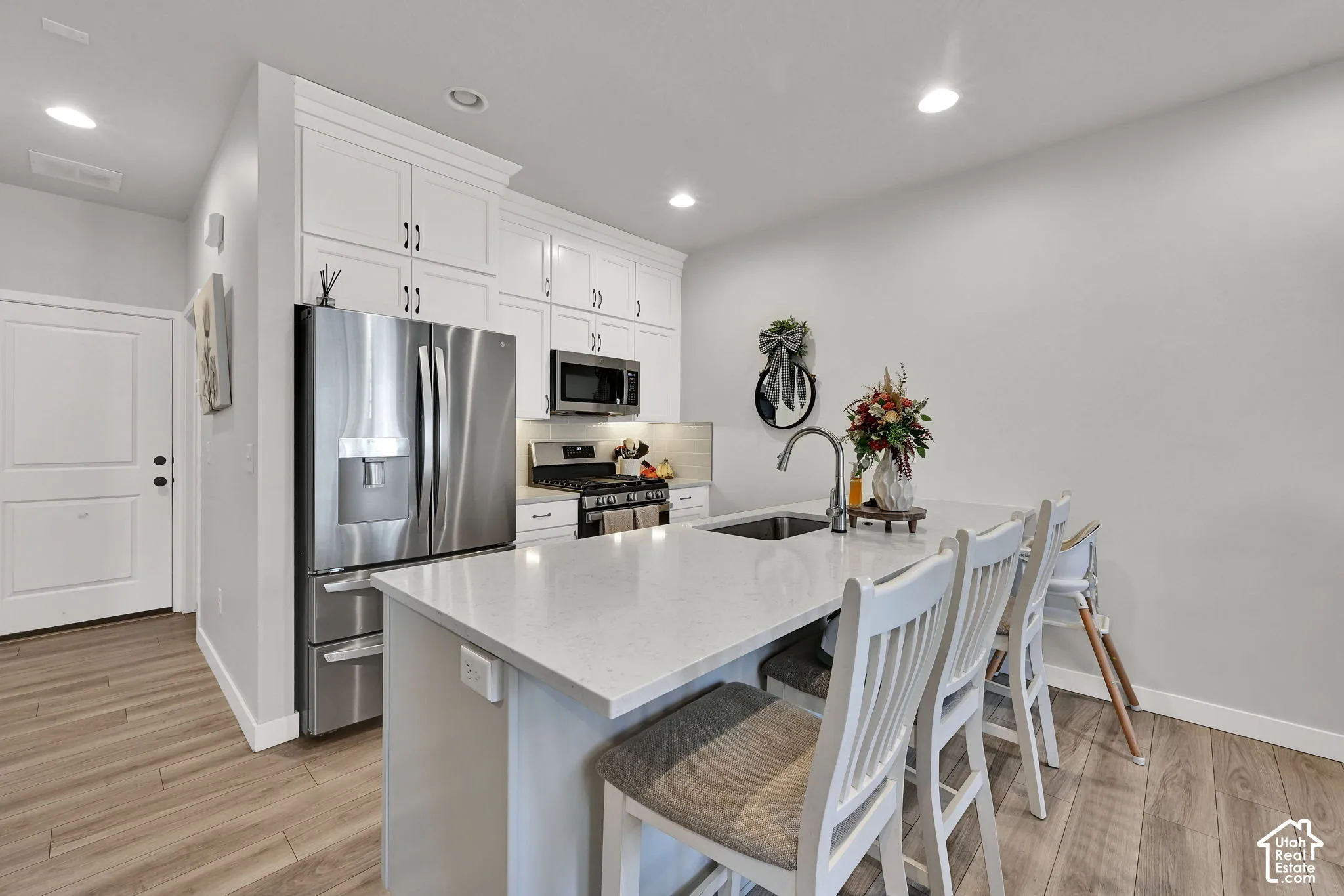 Kitchen featuring an island with a stone-finish countertop, undermount sink, and gooseneck faucet, accompanied by white cabinetry, stainless steel appliances, and wood-finish flooring