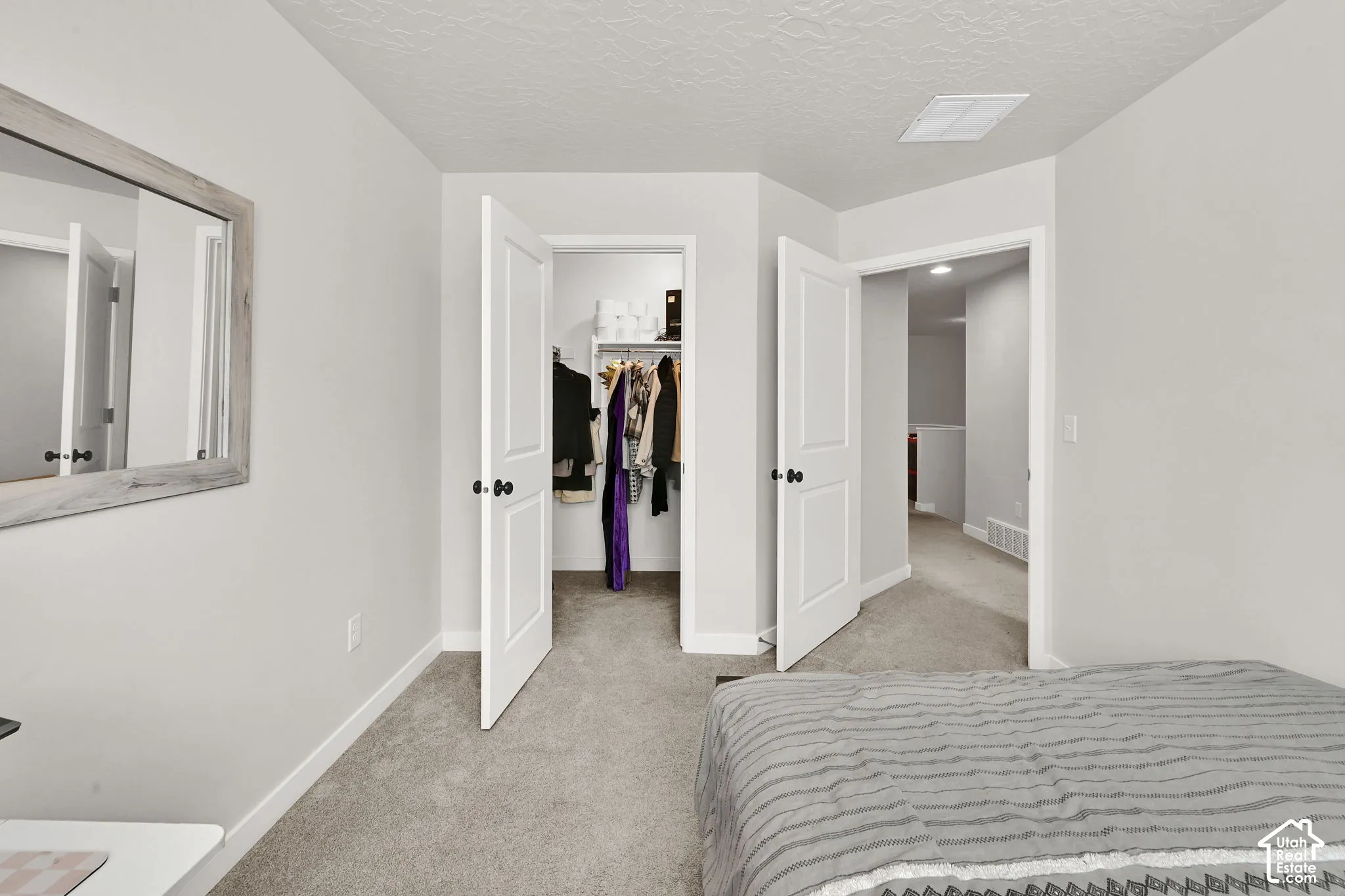 Neutral interior featuring carpeting, a walk-in closet with built-in shelving, two-panel interior doors with matte black hardware, and an attached rectangular mirror