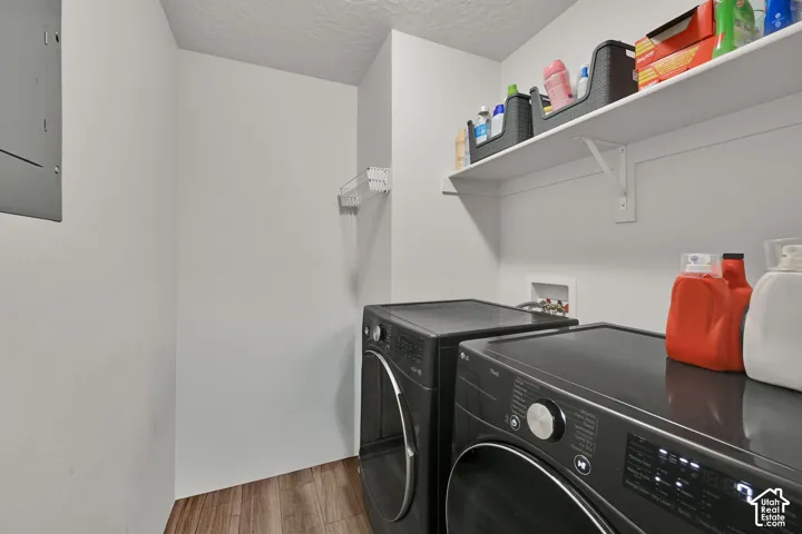 Utility area featuring wood-finish flooring, a wall-mounted shelving unit, and integrated plumbing hookups