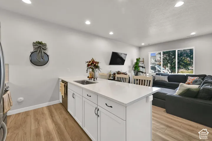 Kitchen island featuring white shaker-style cabinetry, quartz countertops, a stainless steel undermount sink, and wood-finish flooring with recessed lighting