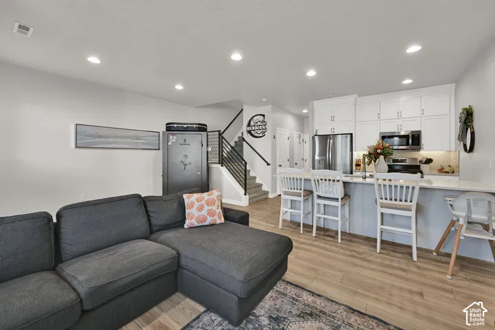 Kitchen featuring white upper cabinetry, stainless steel appliances, breakfast bar island, recessed lighting, and wood-finish flooring