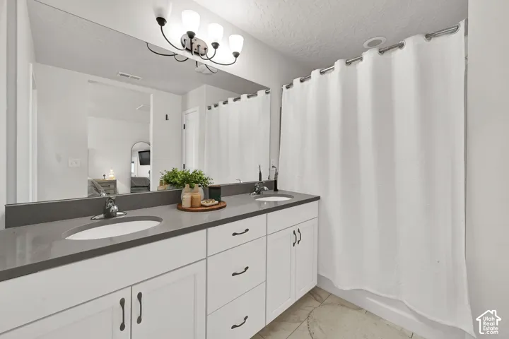 Dual-sink vanity featuring a stone countertop, white cabinetry with dark hardware, a full-width mirror, and multi-bulb wall-mounted lighting