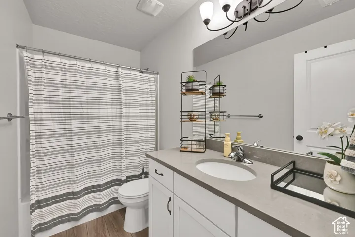 Bathroom featuring a white vanity with a composite countertop, an undermount sink, a full-width mirror, and wood-finish flooring