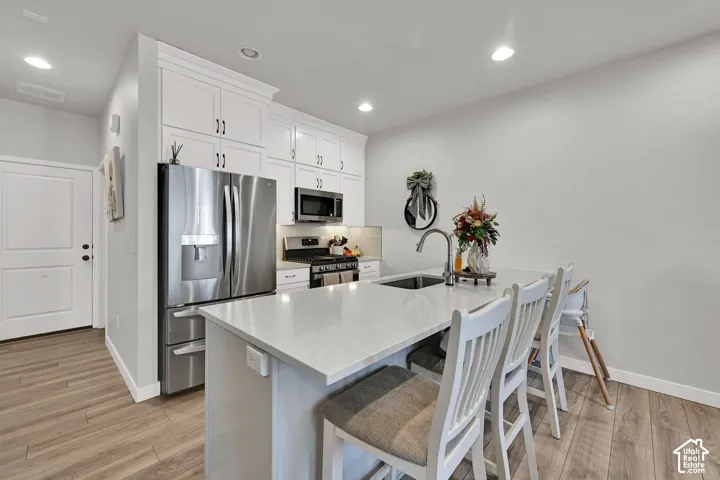 Kitchen featuring an island with a stone-finish countertop, undermount sink, and gooseneck faucet, accompanied by white cabinetry, stainless steel appliances, and wood-finish flooring