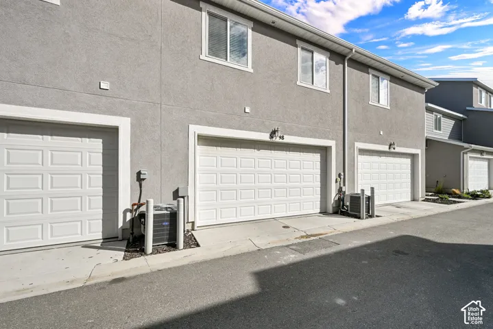 Stucco exterior featuring multiple attached garages with white panel doors, individual HVAC condenser units, and single-hung windows
