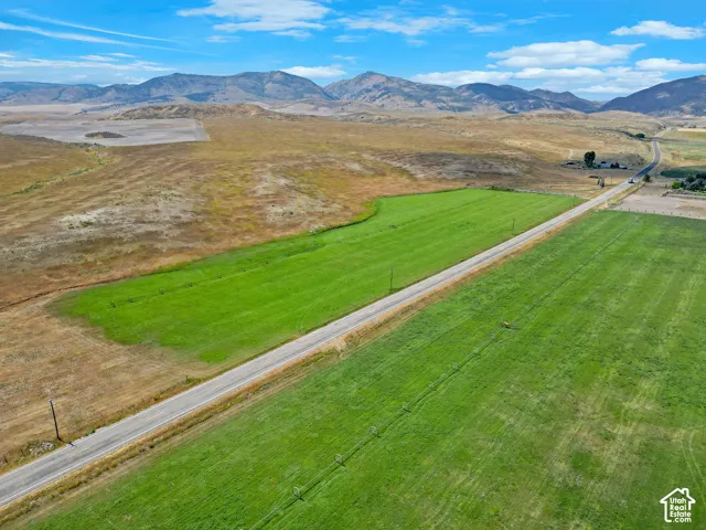 Expansive acreage featuring cleared pasture land, paved road access, utility poles, and mountain backdrops