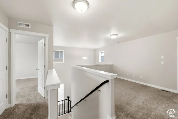 Upper-level landing with neutral carpeting, white trim, and a white balustrade with a black handrail