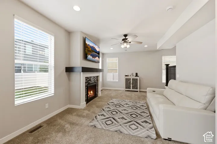 Recessed lighting with a ceiling fan, fireplace with a tiled surround and dark mantel, and multiple windows with blinds