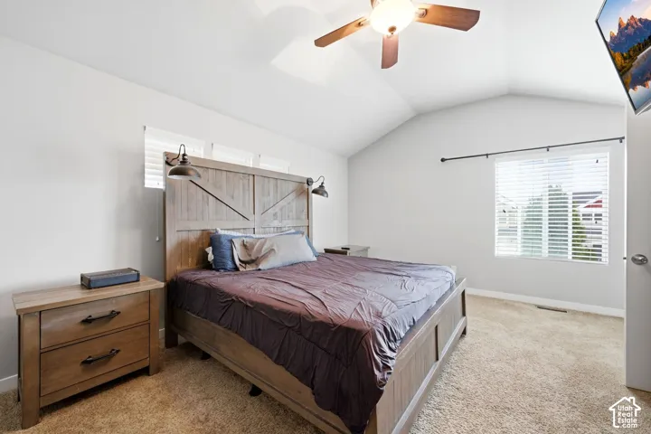 Vaulted ceiling with an attached ceiling fan, wall-mounted light fixtures, and a large window