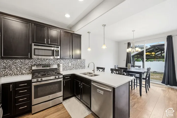 Dark wood-finish cabinetry, stainless steel appliances, mosaic tile backsplash, white countertops, and wood-finish flooring