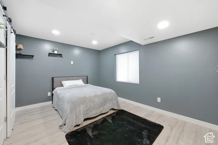 Recessed ceiling lighting, light wood-finish flooring, a window with blinds, and a white sliding barn door