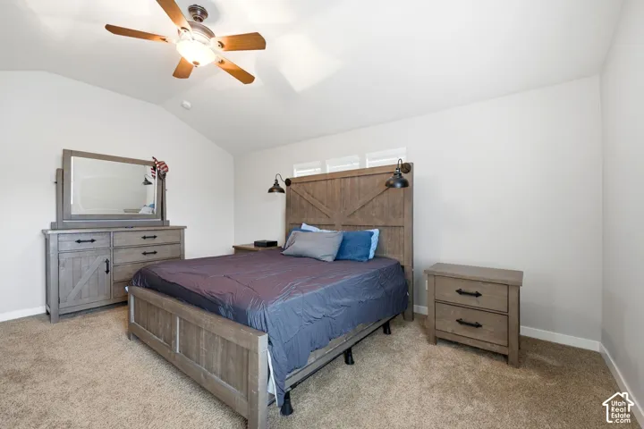 Vaulted ceiling, ceiling fan with light fixture, wall-mounted sconce lighting, carpet flooring, windows with horizontal blinds