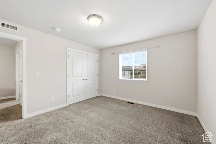 Plush carpet flooring, neutral paint palette, bright overhead lighting, and a double-door closet