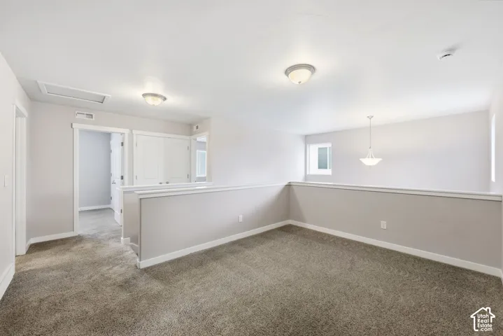 Carpeted loft space with a modern pendant light, flush mount lighting, interior window, and natural light