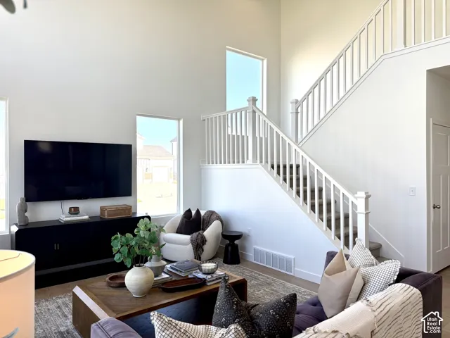 Two-story ceilings, white painted staircase with balusters, light wood-finish flooring, multiple windows, and a built-in media console