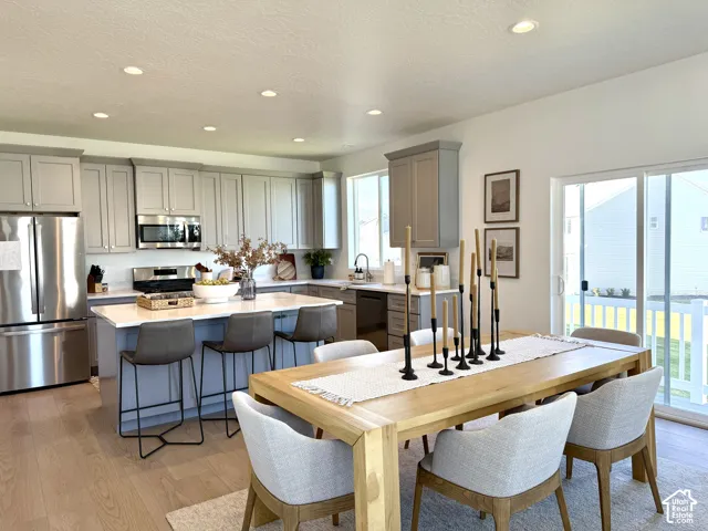 Contemporary kitchen with light wood-finish flooring, stainless steel appliances, recessed lighting, a kitchen island with seating, and a dining area with sliding glass door access