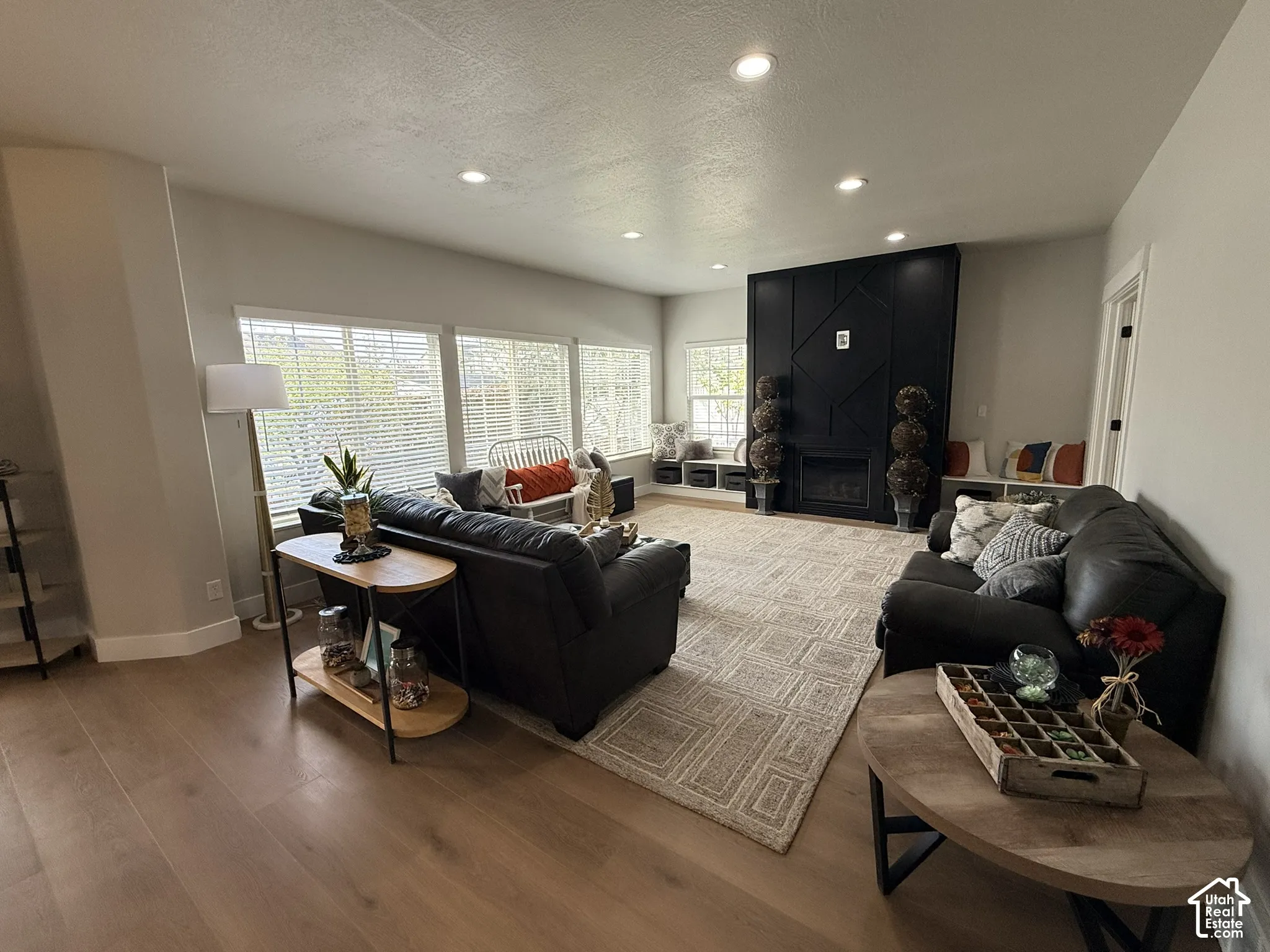 Living area featuring wood-finish flooring, recessed lighting, expansive windows, a floor-to-ceiling accent wall, and a fireplace with built-in bench seating