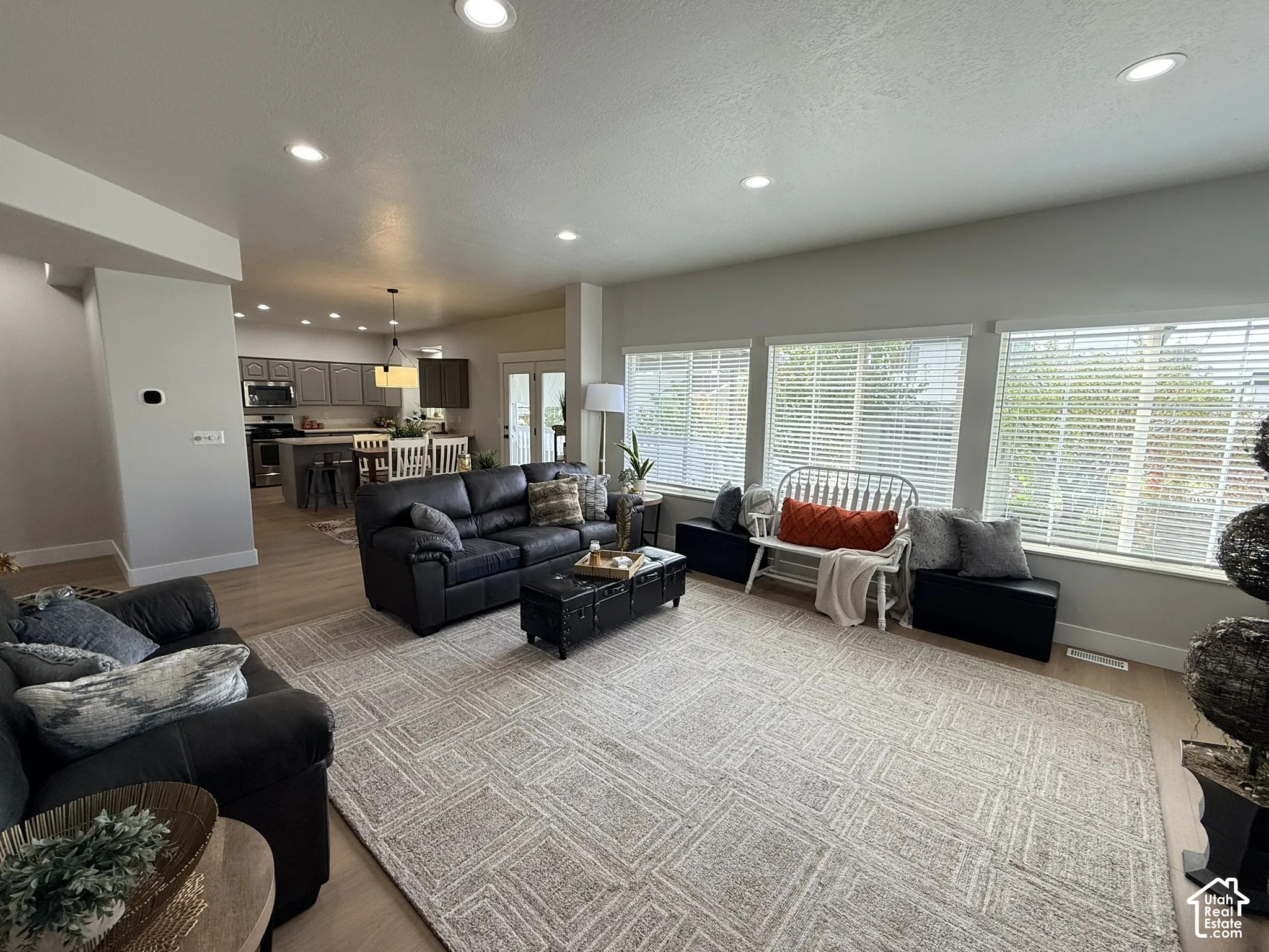 Open-concept living space featuring wood-finish flooring, recessed lighting, and large windows with horizontal blinds