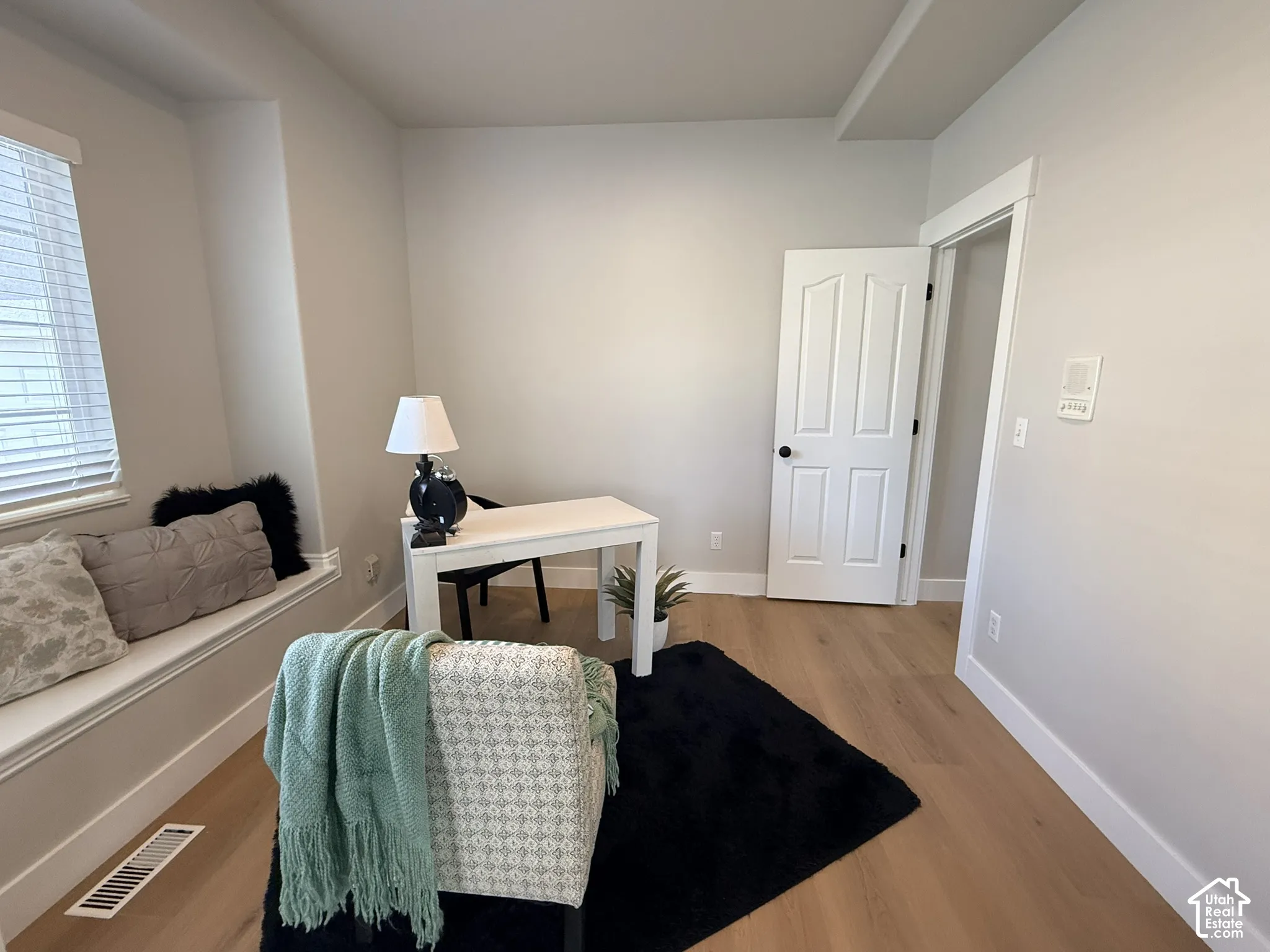 Neutral-toned room featuring light wood-finish flooring, a built-in window seat, and a paneled interior door
