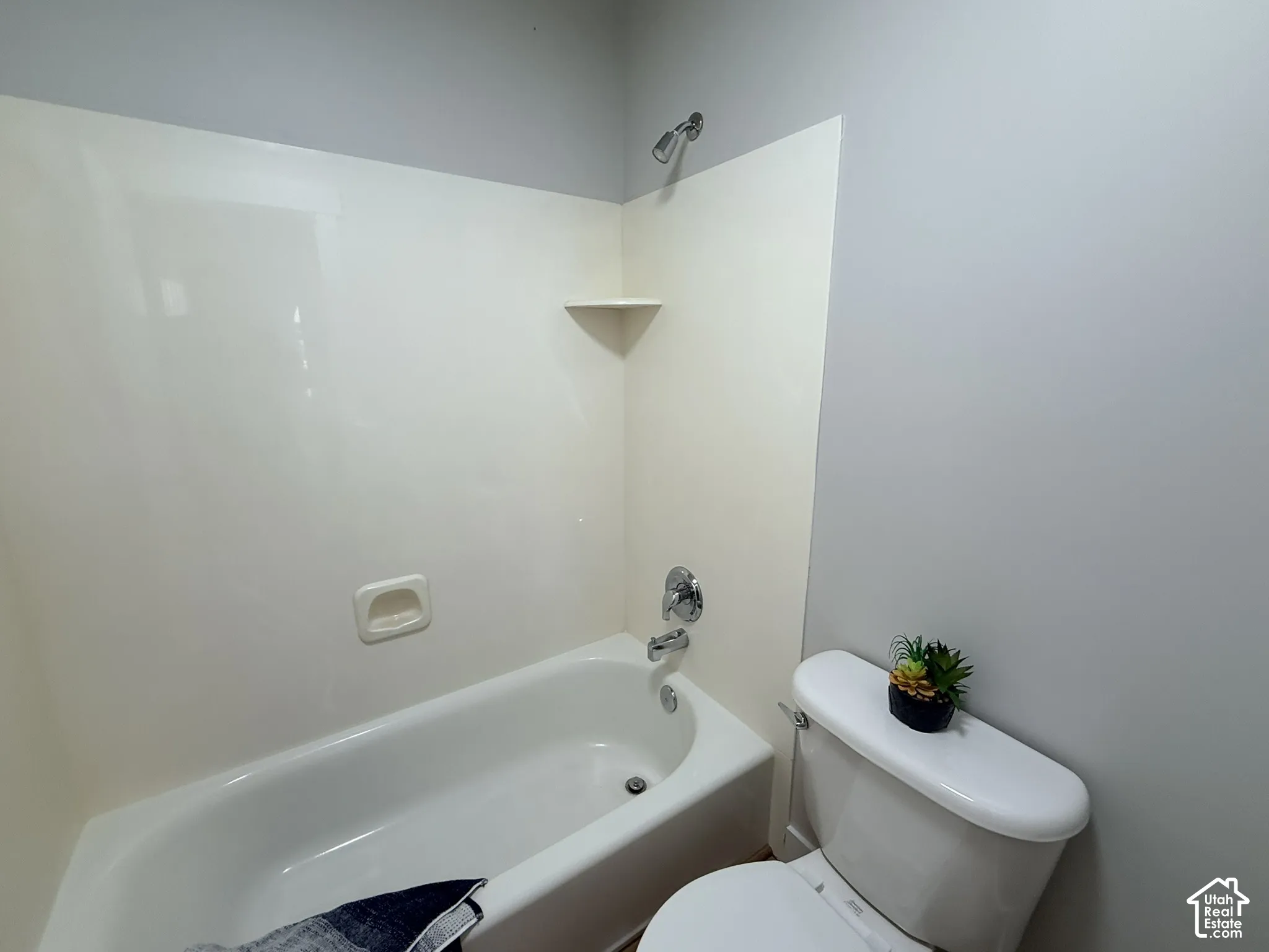 Full bathtub with integrated surround, chrome fixtures, built-in shelving, and a white porcelain toilet