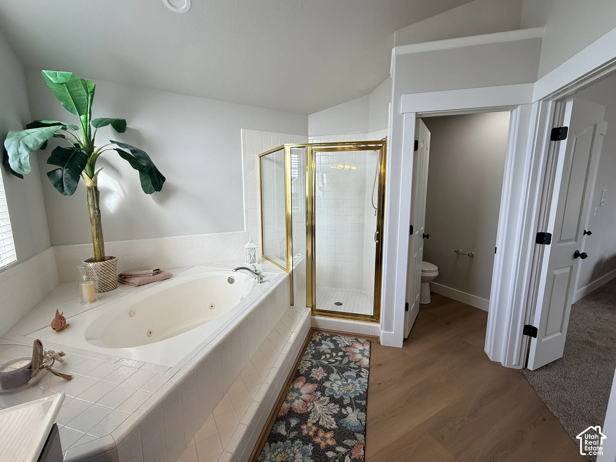 Jetted soaking tub with tile surround, corner glass-enclosed shower with metal frame, wood-finish flooring, and crisp white trim