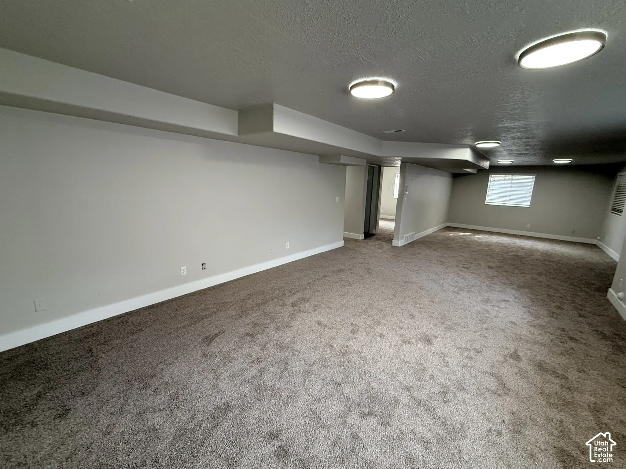 Expansive carpeted area featuring neutral-toned walls, recessed ceiling lighting, and a single window with blinds