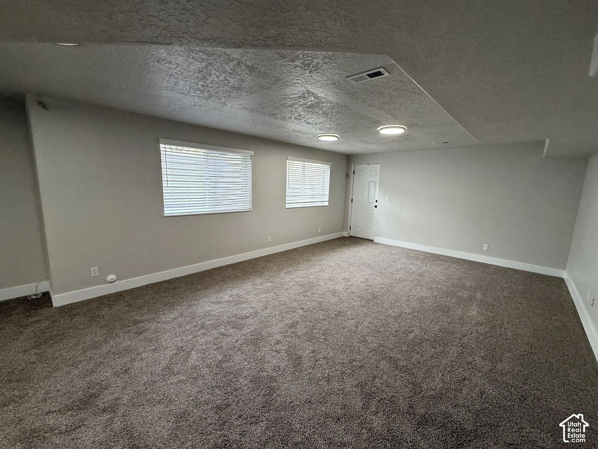 Neutral-toned interior space featuring wall-to-wall carpeting, recessed ceiling lighting, and two windows with horizontal blinds