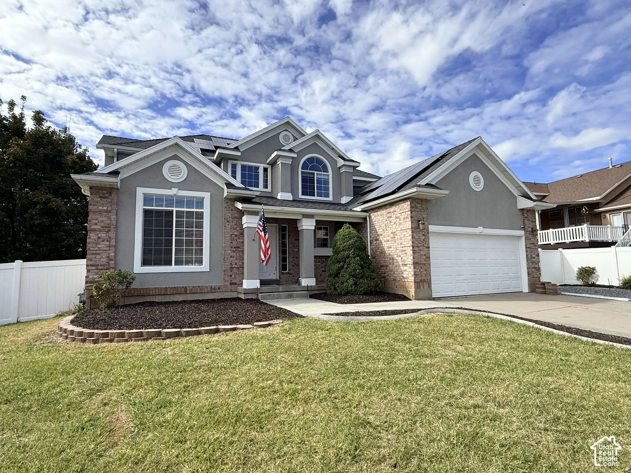 Multi-gabled exterior featuring stucco and brick masonry, solar panel array, attached two-car garage, and tiered stone landscape edging