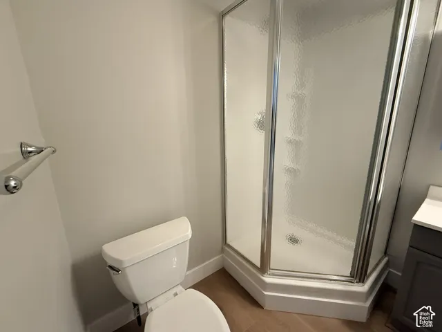 Corner shower enclosure with textured glass doors and chrome hardware, white toilet, wall-mounted chrome towel bar, and charcoal-finish vanity with a white countertop