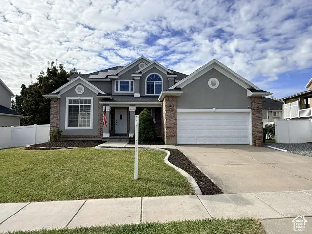 Two-story stucco and brick exterior featuring a multi-gable roofline, an arched dormer window, integrated solar panels, and a two-car garage