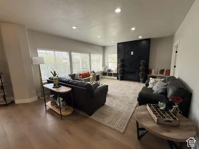 Living area featuring wood-finish flooring, recessed lighting, expansive windows, a floor-to-ceiling accent wall, and a fireplace with built-in bench seating