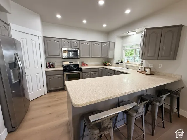 Kitchen featuring light wood-finish flooring, grey cabinetry, stainless steel appliances, speckled solid-surface countertops, and recessed lighting