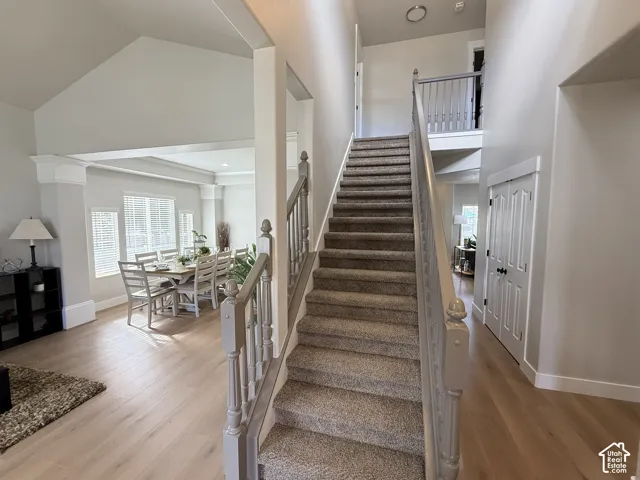 Vaulted ceiling entryway featuring carpeted staircase with wood banister, wood-finish flooring, and double-panel closet doors