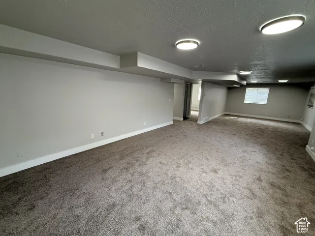 Expansive carpeted area featuring neutral-toned walls, recessed ceiling lighting, and a single window with blinds