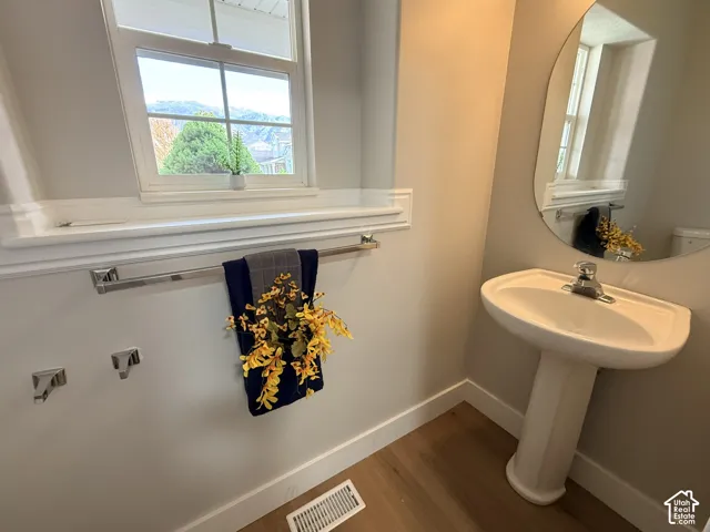 Pedestal sink with a polished chrome faucet, oval wall-mounted mirror, wood-finish flooring, and window with extensive trim molding
