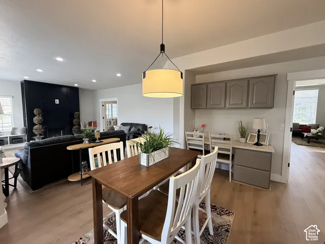 Open-concept area featuring wood-finish flooring, a contemporary drum pendant light, a built-in workstation with neutral-toned cabinetry, and a floor-to-ceiling dark-toned fireplace surround