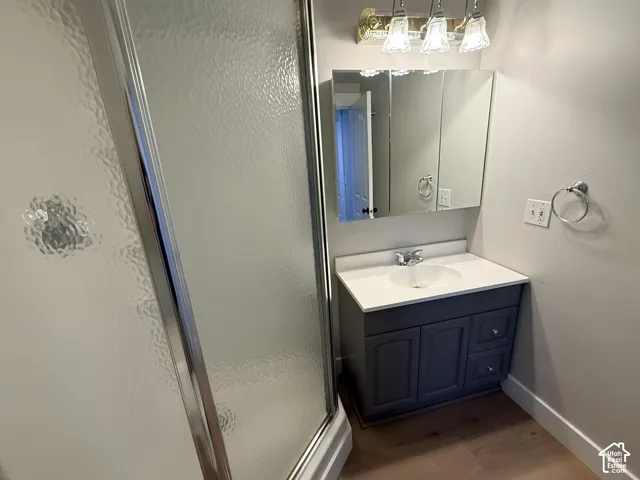 Bathroom featuring a wood-finish vanity with a white countertop, chrome-finish faucet, tri-fold mirrored medicine cabinet, and glass-enclosed shower