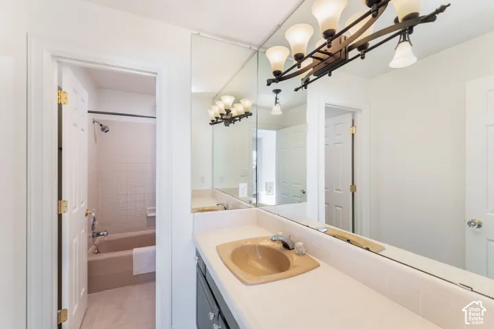 Vanity featuring a solid-surface countertop with an integrated basin, full-width wall mirror, five-light fixture with frosted glass shades, and a separate tub and shower combination with tile surround