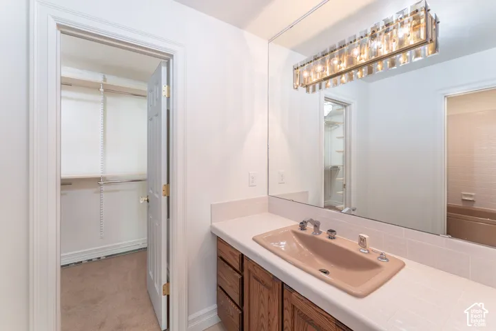 Bathroom featuring a wood-finish vanity cabinet, light-toned tile countertop, integrated basin, large wall-mounted mirror, and tiered glass light fixture